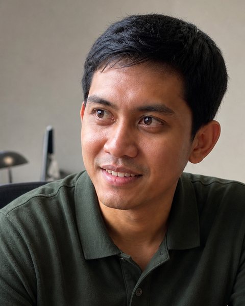 Bayu Nugraha, a man with short black hair in a dark green polo shirt, at a desk with a laptop